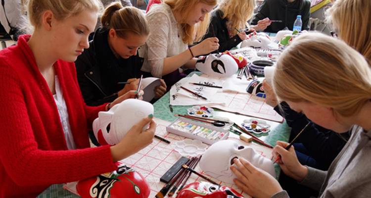 Groupe de personnes peignant des masques autour d'une table.