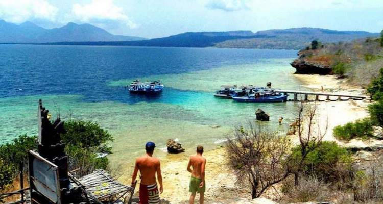 Deux personnes debout sur la plage avec des bateaux et une vue sur l'océan bleu.