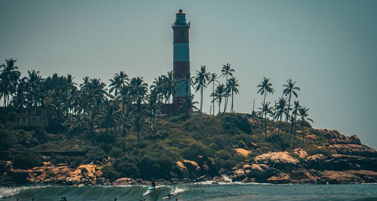 Lighthouse on a coastal cliff surrounded by palm trees.
