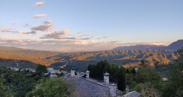 Vue en début de soirée sur des toits en tuiles orientés vers les montagnes vertes ondulantes sous des nuages légers.