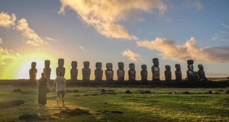 Pareja tomada de la mano al atardecer frente a la larga fila de estatuas moái en Ahu Tongariki.