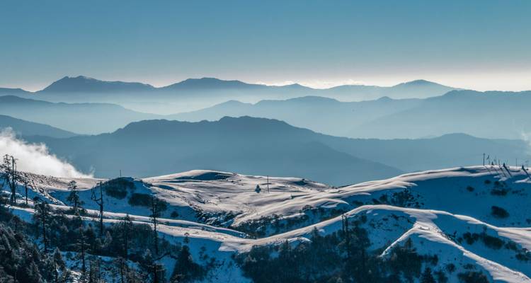 Verschneite Landschaft mit gestaffelten Gebirgszügen in der Ferne.