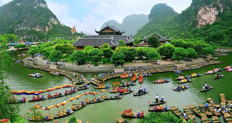 Colorful boats on a river with people paddling, surrounded by lush greenery.