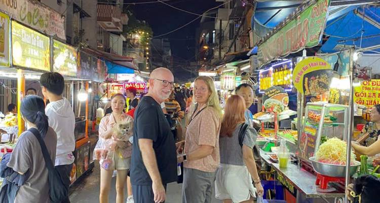 Crowded night market with food stalls and people walking.
