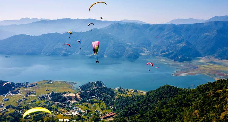Paragliders in the sky with a scenic landscape below.