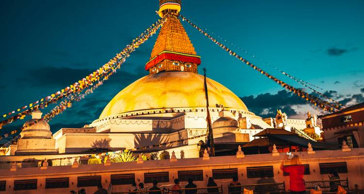 Stupa glowing at night with prayer flags and visitors.