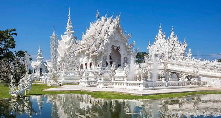 White temple with intricate architecture and reflection in a pond.
