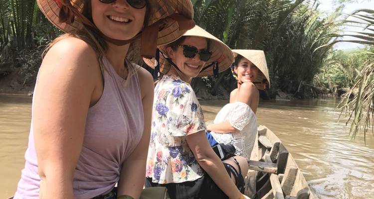 Drie vrouwen zittend in een traditionele boot op een modderige rivier.