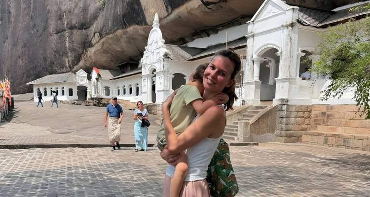 Woman holding a child outside white temple buildings.