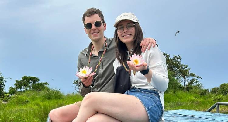 Couple on a boat holding lotus flowers in a serene setting.