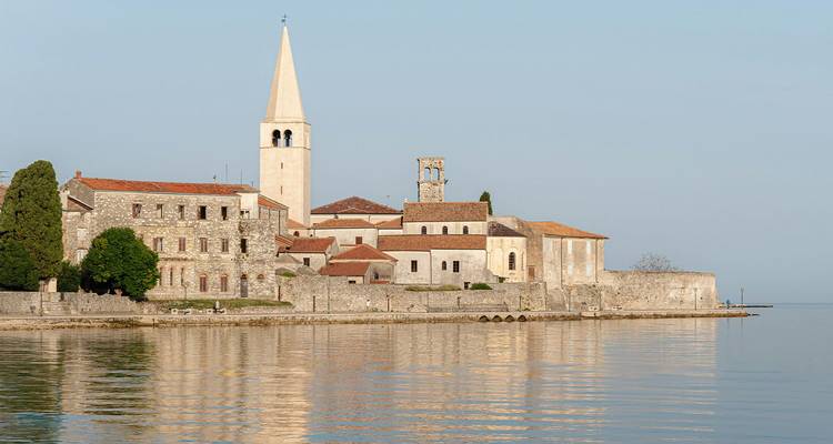Ruhiger Küstenkirchencomplex mit hohem Glockenturm, der sich in den ruhigen Gewässern der Adria bei Poreč spiegelt.