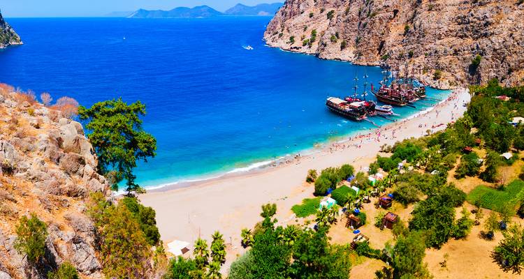 Plage avec des bateaux et des eaux bleues claires entourée de falaises.