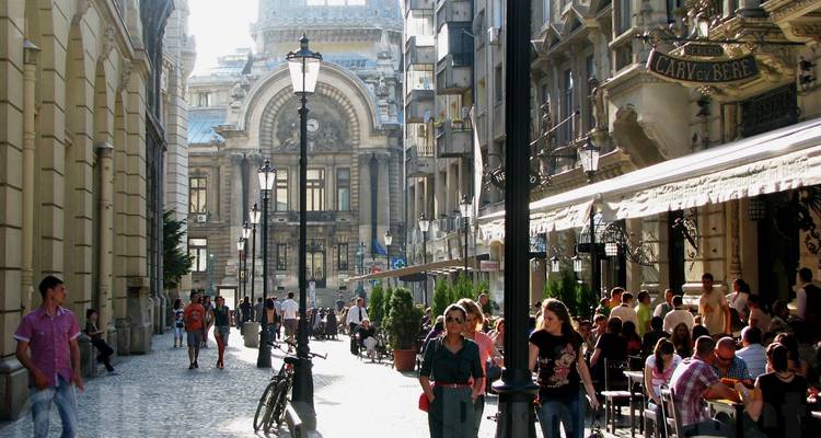 Une rue animée avec des gens qui marchent et qui sont assis aux terrasses de cafés.