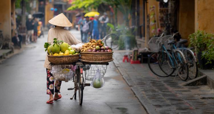 Verkäufer, der ein Fahrrad mit Obstkörben durch eine Stadtstraße schiebt.