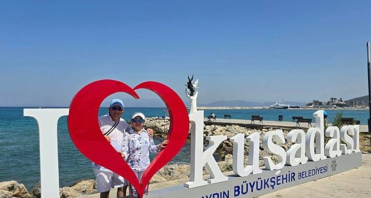 Pareja posando con un gran letrero de Kusadasi junto al mar.