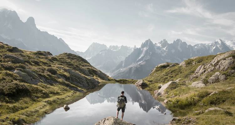 Randonneur admirant une vue de montagne reflétée dans un petit lac.