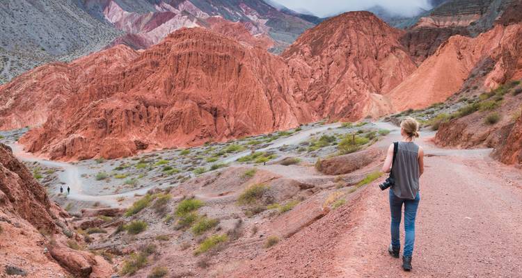 Persona caminando por terreno montañoso con una cámara.
