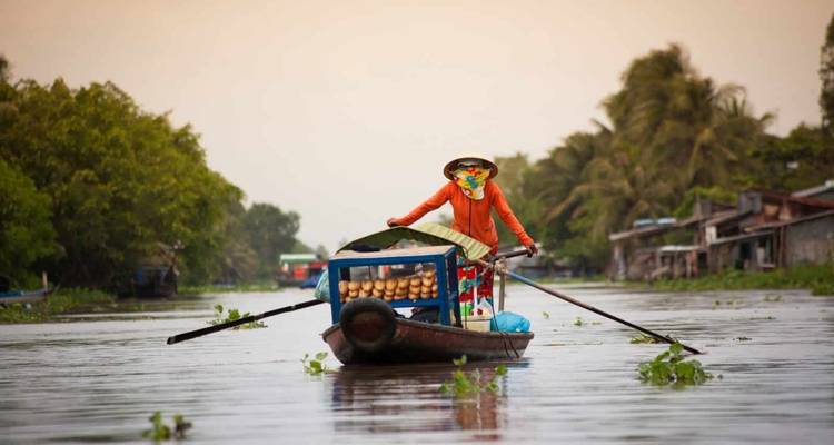 Een persoon die een boot peddelt op een rivier omzoomd met groen.