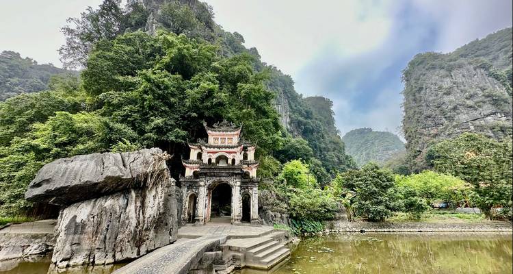 Een schilderachtig uitzicht op de ingang van een tempel genesteld tussen weelderige groene bergen met een vijver op de voorgrond.