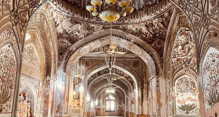 Interior de mezquita lujosamente decorado con frescos intrincados y arcos que conducen a una puerta luminosa