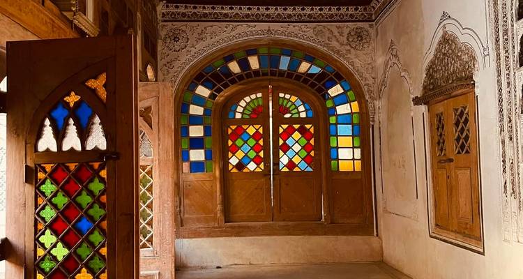 Habitación con paredes de estuco de patrones ricos y vibrantes ventanas de vidrio emplomado que proyectan luz de colores