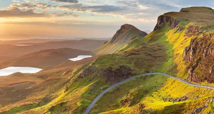 Sweeping vista of the Quiraing on the Isle of Skye with winding road and lochs at golden hour.