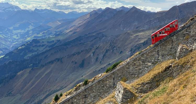 Tren de cremallera rojo en una vía montañosa empinada con vistas panorámicas.