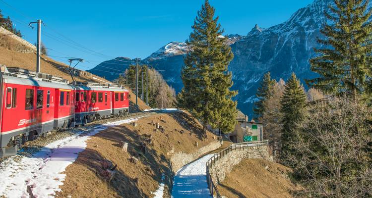 Tren rojo viajando a través de un paisaje montañoso con nieve y árboles.