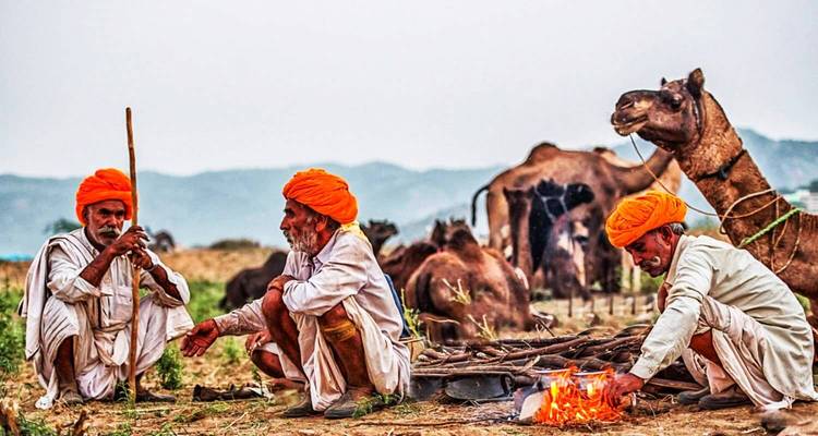 Een groep mannen die tulbanden dragen, zittend rond een vuur met kamelen op de achtergrond.