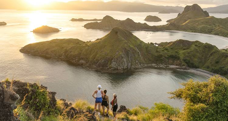 Wandelaars genieten van een gouden zonsondergangzicht over de ruige eilanden en baaien van Komodo National Park.