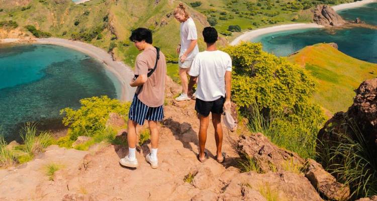 Drei Rucksacktouristen bewundern die weitläufigen Aussichten auf eine Insel und eine türkisfarbene Bucht von einem felsigen Grat aus.