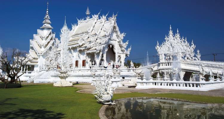 Brilliant white ornate Wat Rong Khun temple complex gleaming under a deep blue sky