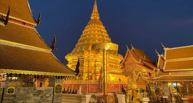 Golden chedi and temple buildings of Wat Phra That Doi Suthep illuminated against the evening sky