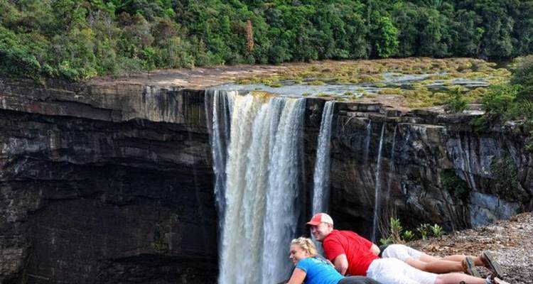 Tourists lying on a ledge overlooking a large waterfall.