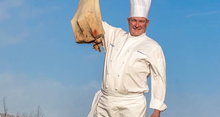 Professionele chef in uniform met gerookt vlees in de hand.