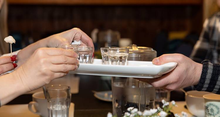 Handen die shotglazen vasthouden op een dienblad in een eetomgeving.