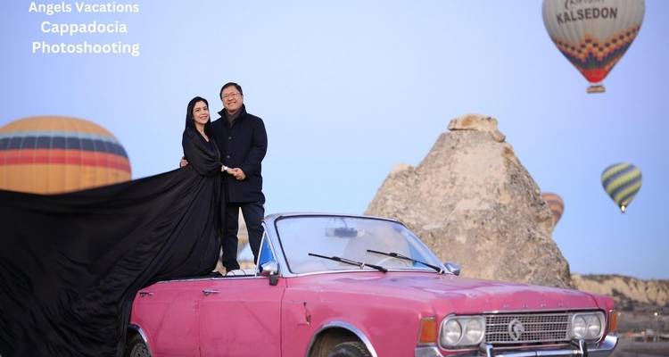 Pareja posando en el techo de un auto vintage rosa bajo el cielo lleno de globos de Capadocia con texto publicitario presente