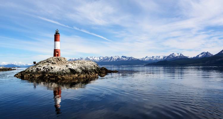 Vuurtoren op een rotsachtig eilandje omgeven door kalm water en een bergketen.