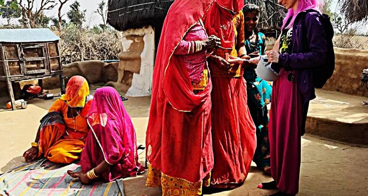 Femme en tenue colorée interagissant avec les habitants dans un cadre de village.