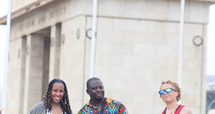 Trois voyageurs souriants pour un portrait avec l'Arche de l'Indépendance d'Accra floue en arrière-plan.