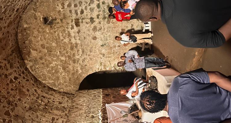 Un groupe de touristes écoute un guide à l'intérieur d'un cachot de pierre sombre avec des plafonds voûtés.