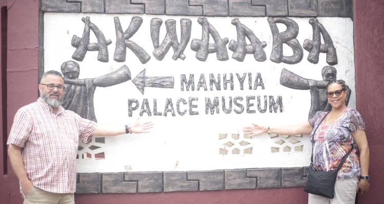 Deux visiteurs posent à côté d'un grand panneau indiquant « Akwaaba – Manhyia Palace Museum » à Kumasi.