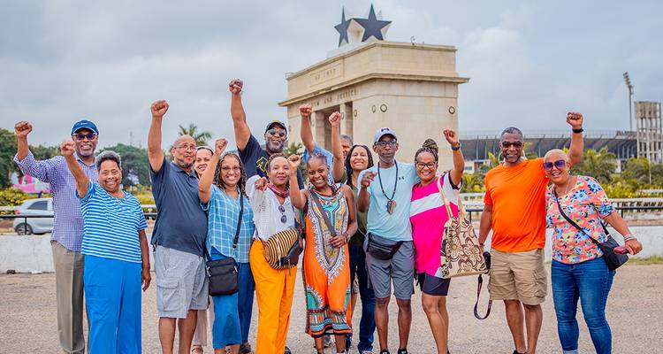 Fröhliche Reisegruppe erhebt die Fäuste in Solidarität vor dem Unabhängigkeitsbogen, der mit einem schwarzen Stern gekrönt ist, in Accra.
