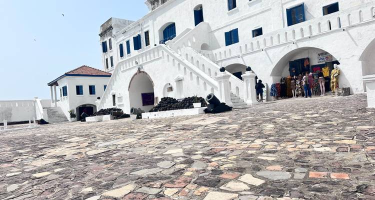 Weiß getünchte Festungsmauern, Kanonen und gewölbte Treppen von Cape Coast Castle, gesehen vom gepflasterten Innenhof.