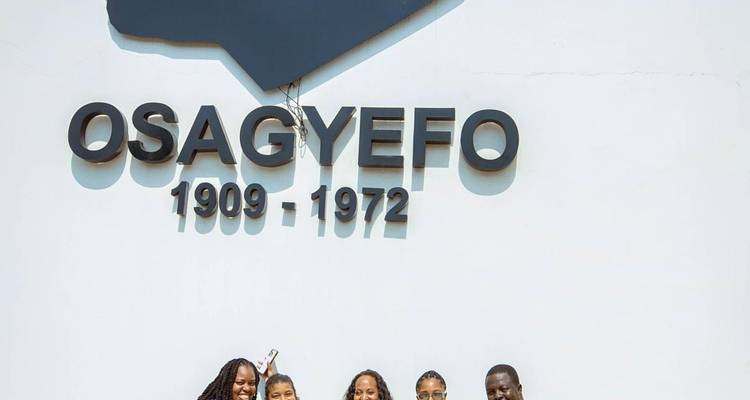 Reisende lächeln unter einer Wandinschrift, die Osagyefo Kwame Nkrumah ehrt, datiert 1909-1972.