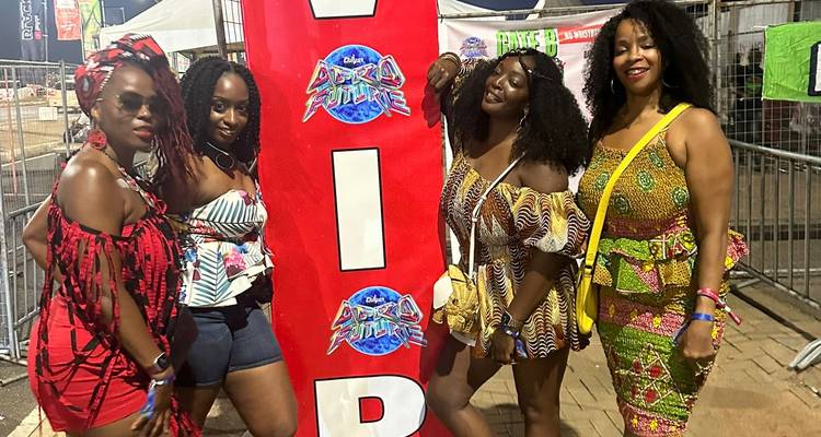 Vier stilvolle Frauen posieren vor einem leuchtend roten VIP-Banner an einem Outdoor-Festivalgelände.