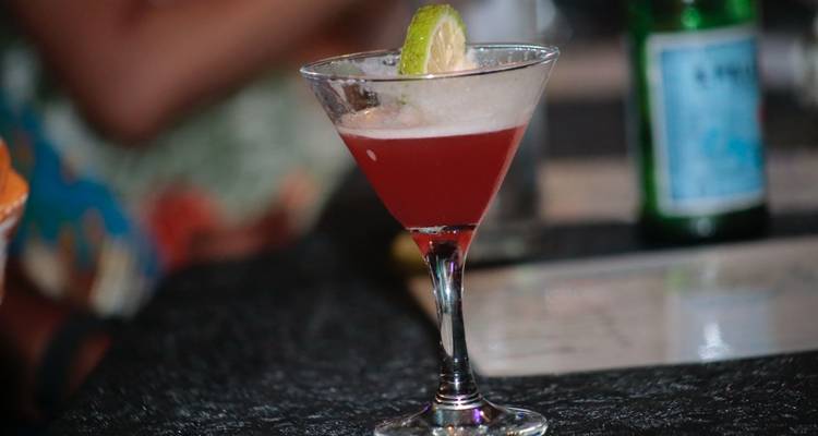 Eleganter roter Cocktail garniert mit einer Limettenscheibe serviert in einem Martiniglas an einer schwach beleuchteten Bar.