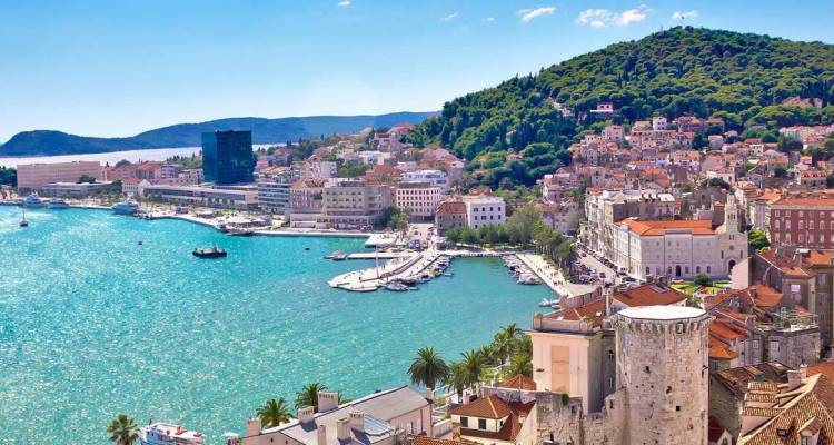 Paisaje urbano costero vibrante con un puerto histórico, mar turquesa y tejados de terracota respaldados por colinas