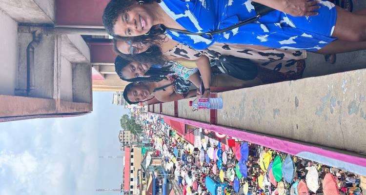 Reisende, die von einem erhöhten Gehweg aus auf die sich ausbreitenden bunten Dächer von Kumasis Kejetia-Markt blicken.