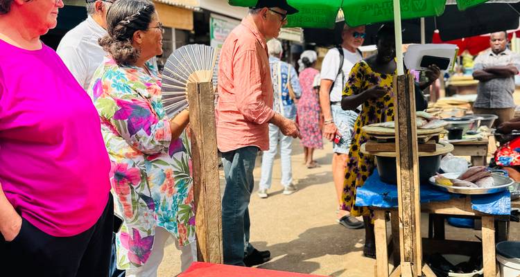 Touristen interagieren mit Verkäufern zwischen geschäftigen Marktständen im Freien, die von Sonnenschirmen beschattet werden.